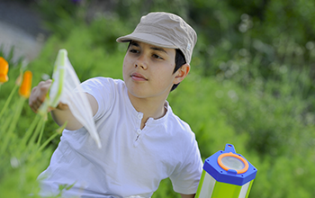 Boy in brown hat swatting a net to catch a butterfly in a field